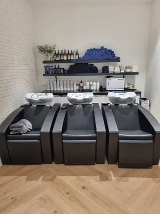 Una peluquería con tres sillas y tres lavabos.