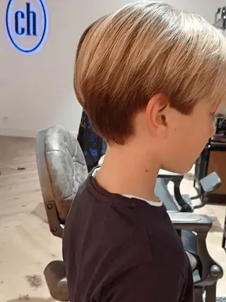 Un niño pequeño está sentado en una silla con el pelo cortado.