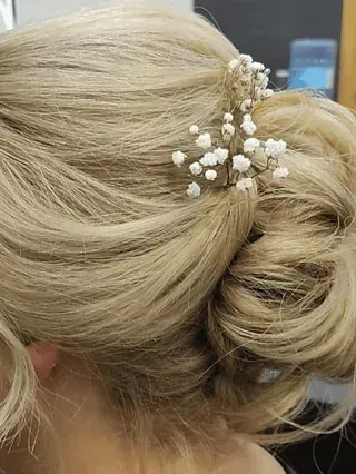 Una mujer con cabello rubio recogido en un moño y con flores de velo en el cabello.