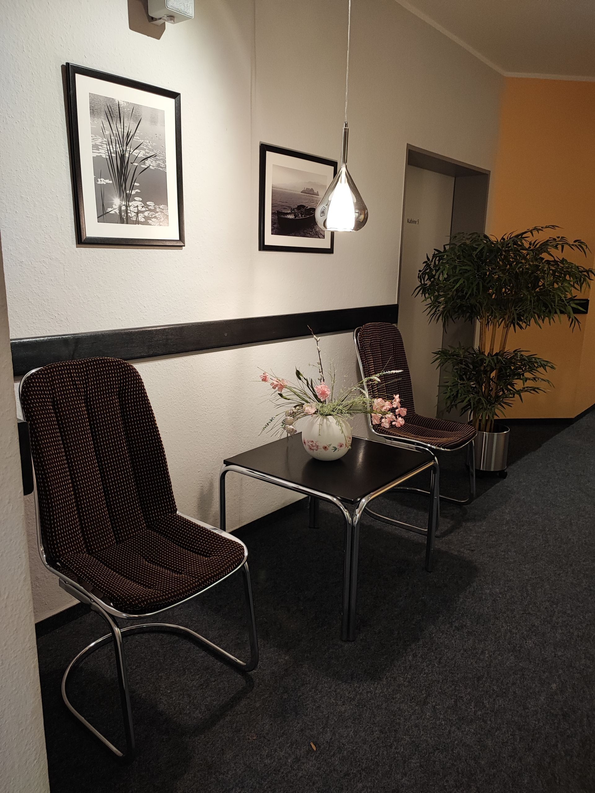 Ein Flur mit zwei Stühlen, einem kleinen Tisch, Kunstwerken und einer Hängelampe.