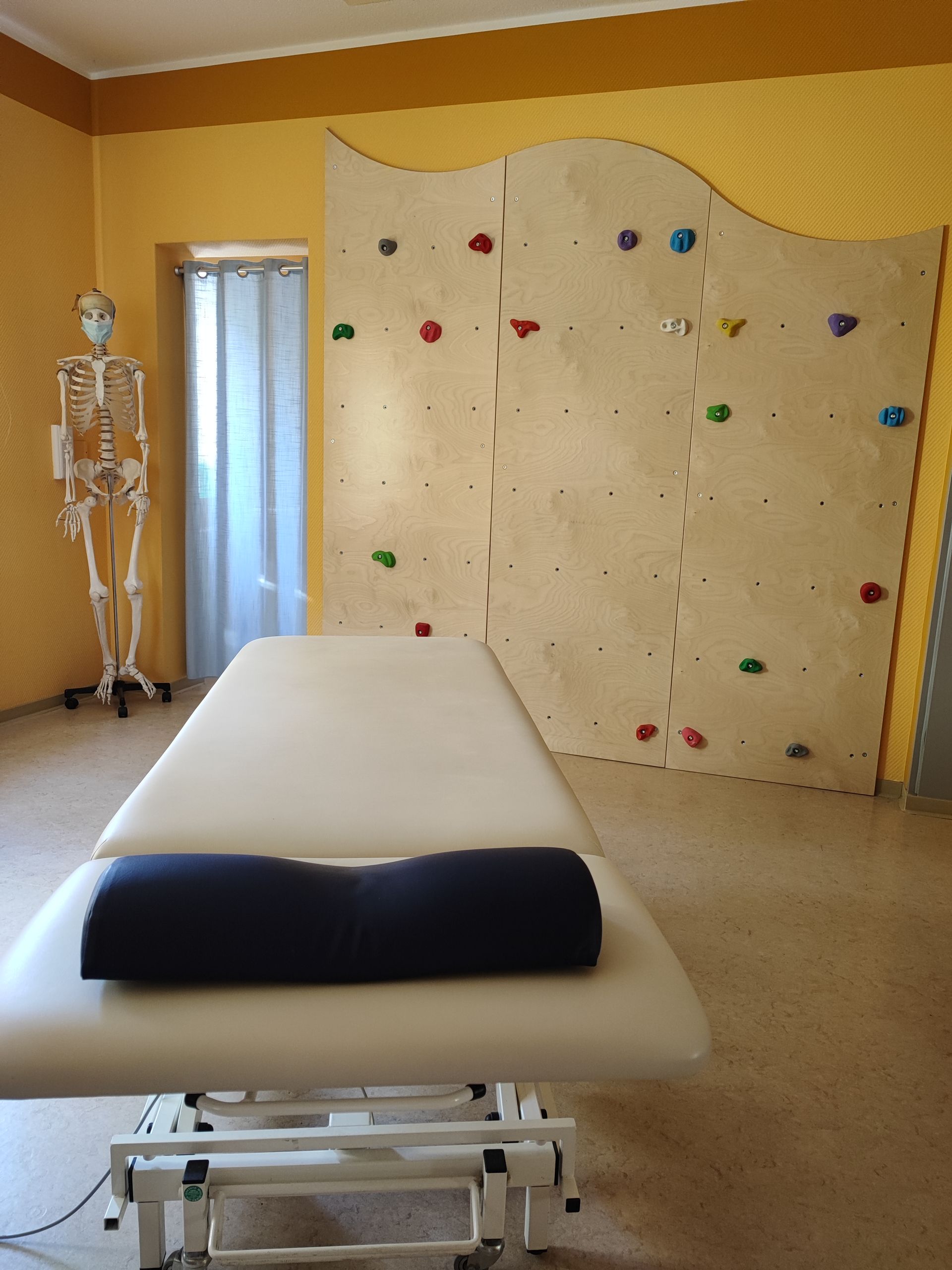 Therapieraum mit Behandlungsliege, Kletterwand und Skelett.