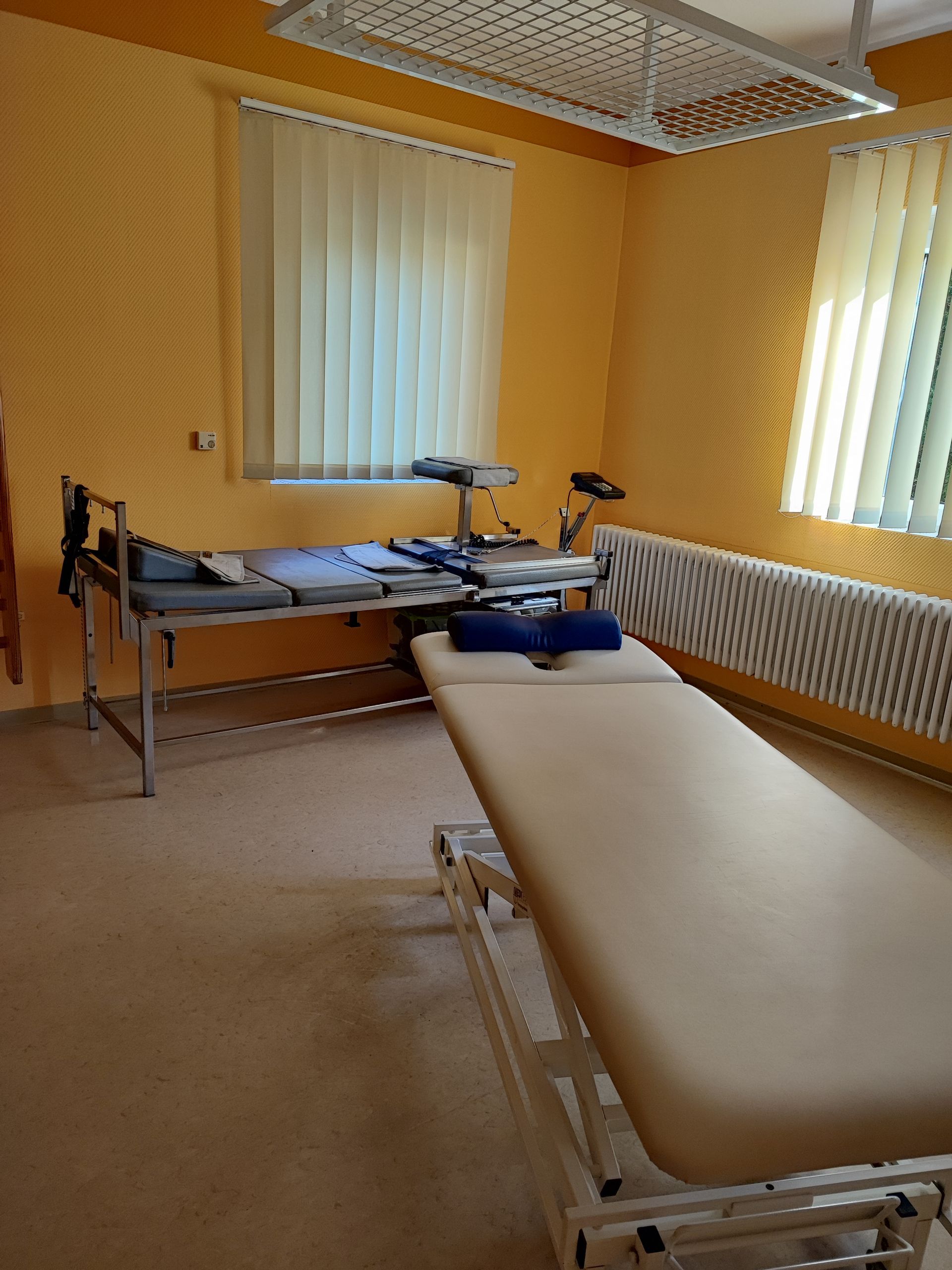 Untersuchungszimmer mit zwei Betten, Jalousien und gelben Wänden.