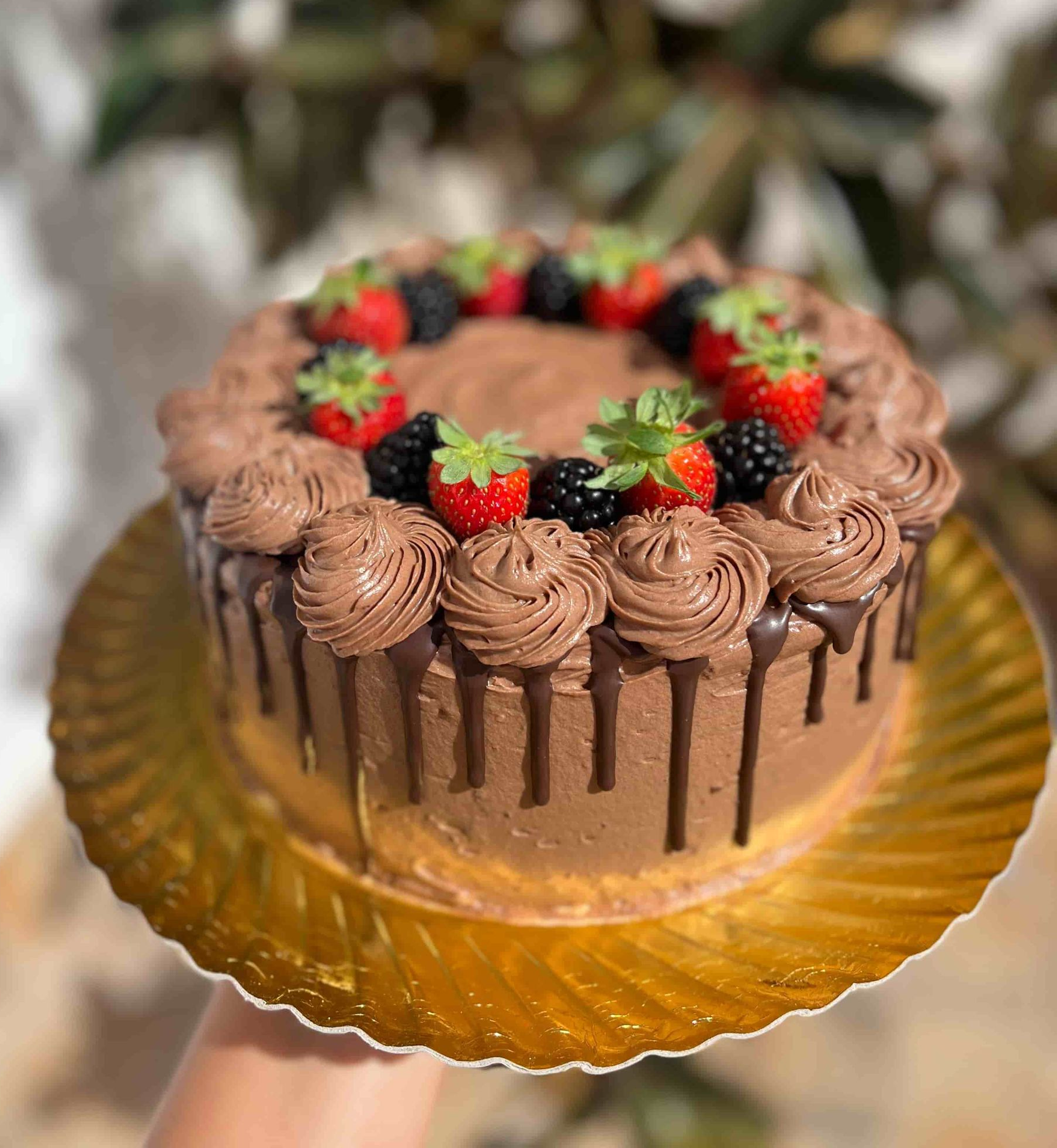 Pastel de chocolate con remolinos de glaseado, gotas y bayas sobre una tabla de servir dorada.