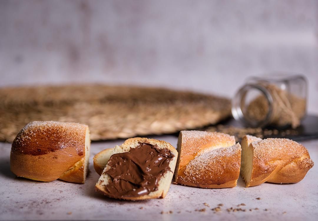 Panecillo en rodajas relleno de chocolate, semillas de sésamo y azúcar espolvoreado sobre una mesa.