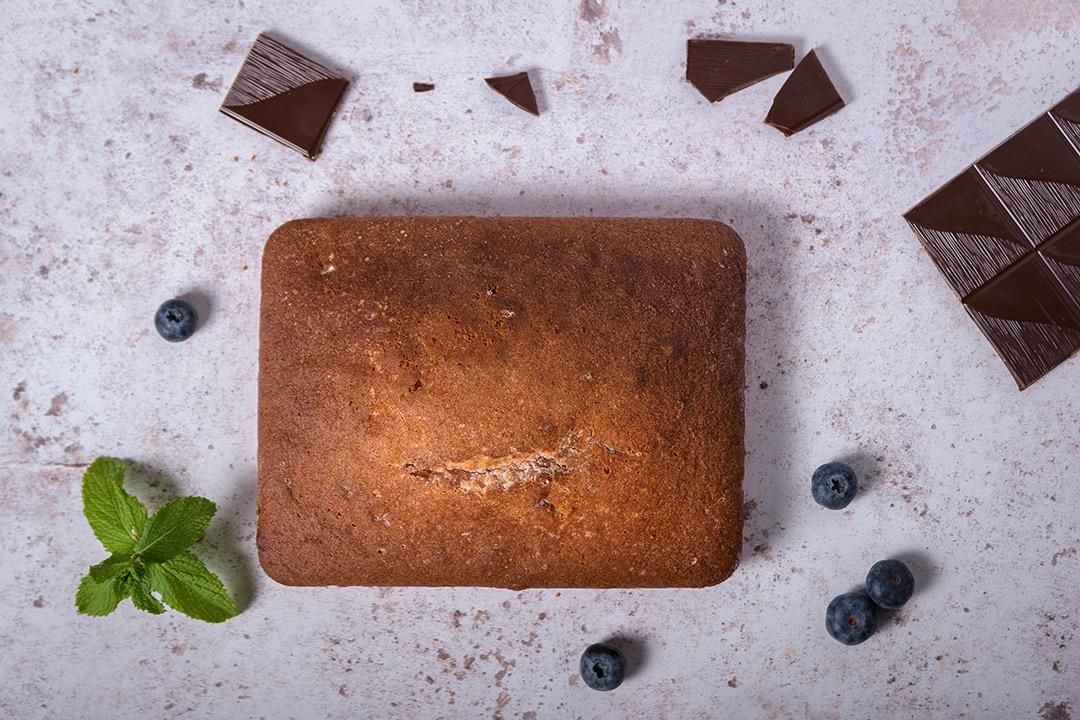 Pastel cuadrado con arándanos, trozos de chocolate y menta sobre una superficie texturizada.