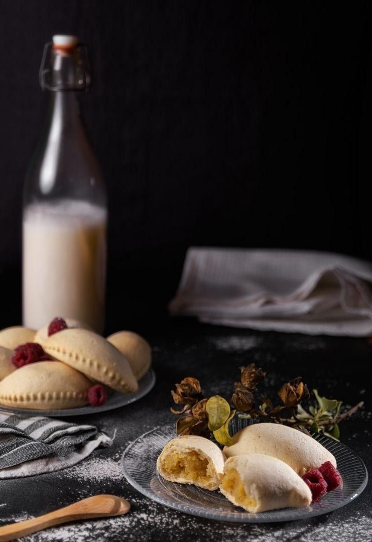 Cuatro pasteles de color marrón dorado con forma de campana y puntas de almendra, alineados sobre una superficie oscura.