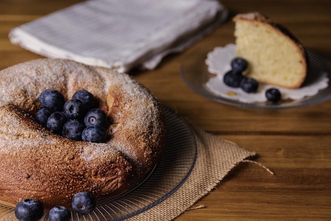 Pastel con arándanos sobre una mesa de madera, una rebanada de pastel en un plato y un mantel en el fondo.