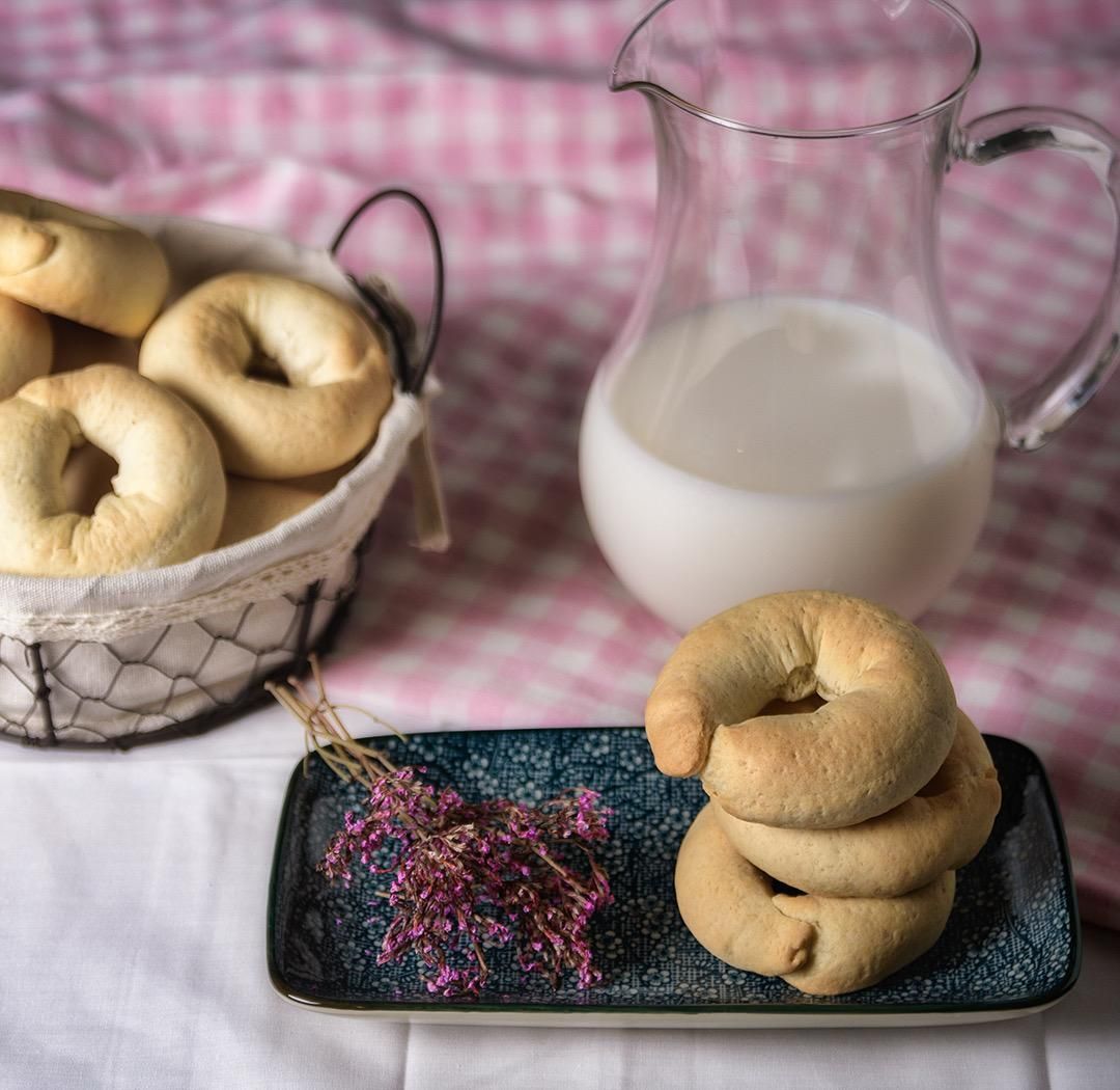 Bagels, jarra de leche y cesta sobre un mantel a cuadros. Montón de bagels en un plato pequeño con flores.