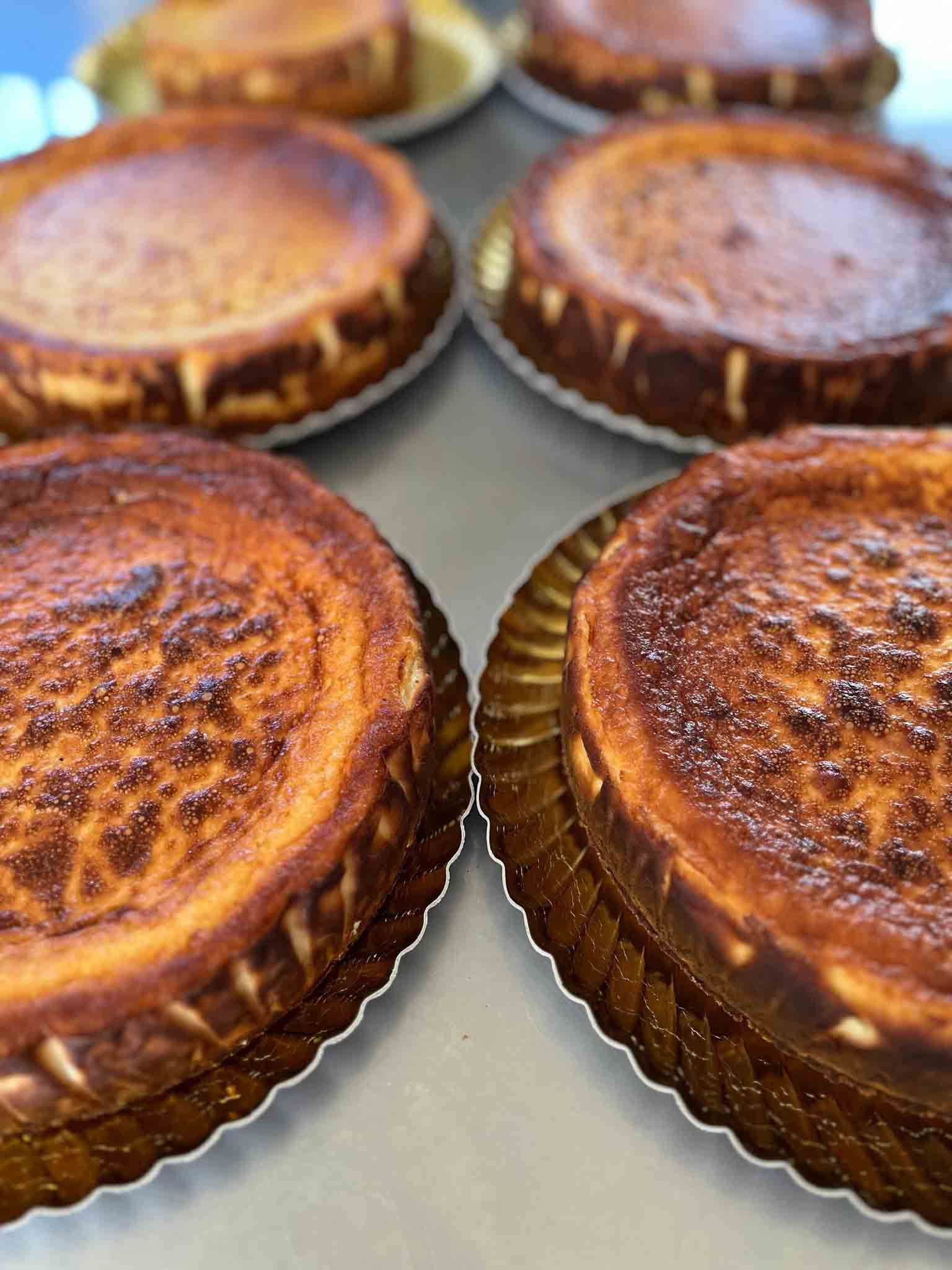 Primer plano de varias tartas de queso vascas de color marrón dorado sobre platos dorados decorativos.