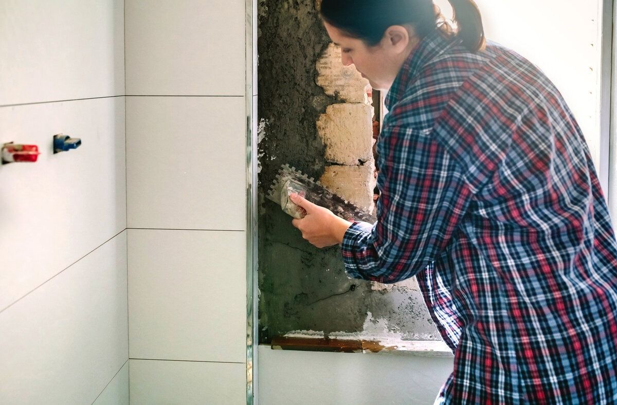 Una mujer con una camisa a cuadros está trabajando en la pared de un baño.