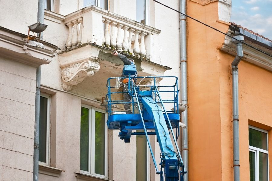 Un hombre está pintando el costado de un edificio con una grúa.