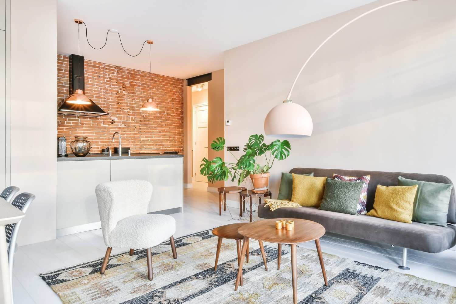 Sala de estar moderna con sofá gris, sillón blanco, mesa de centro de madera y cocina abierta con detalles en cobre.