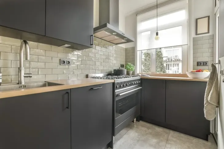 Cocina moderna con armarios oscuros, encimeras claras, estufa, salpicadero de azulejos y una ventana luminosa.