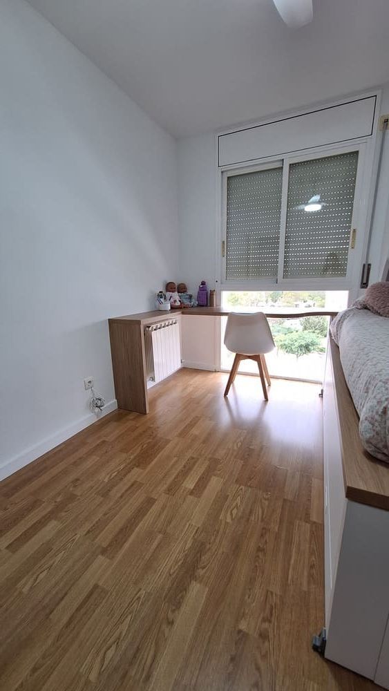 Habitación con suelo de madera, escritorio, silla y cama cerca de una ventana con persiana cerrada.