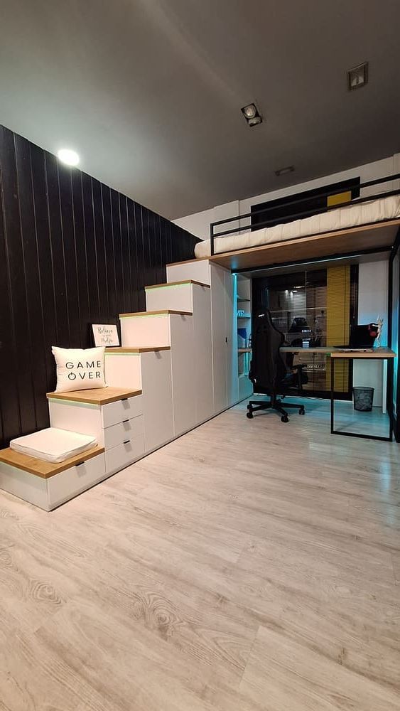 Dormitorio moderno tipo loft con espacio de almacenaje en la escalera, escritorio y cama elevada. Predominan los tonos negro, blanco, gris y madera.