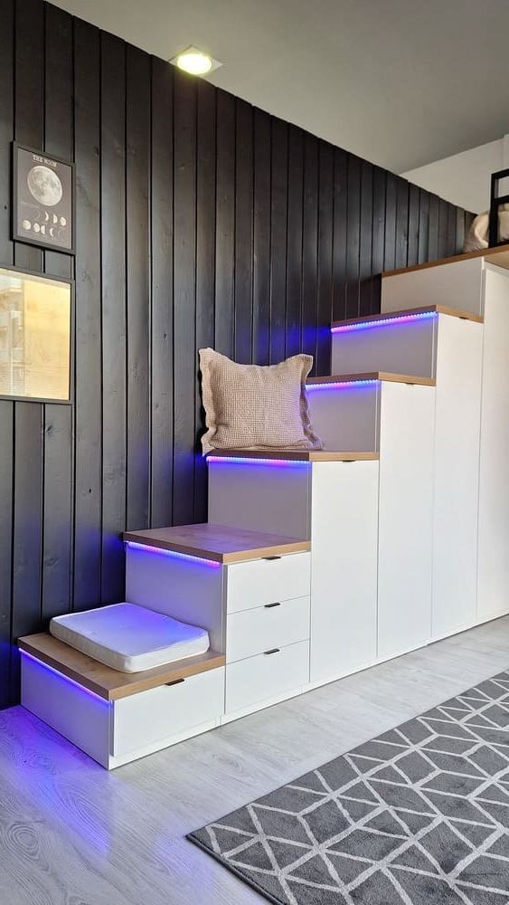 Mueble de almacenaje en forma de escalera con cajones, iluminación incorporada, escalones de madera, contra una pared de madera oscura.