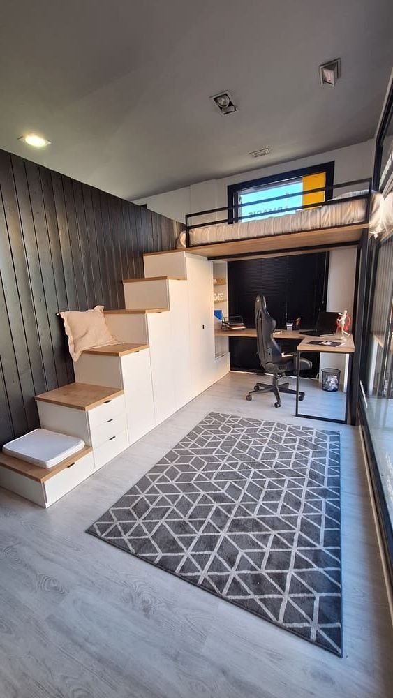 Cama alta en un apartamento pequeño con escalera y espacio de almacenamiento incorporado. Hay un escritorio debajo.