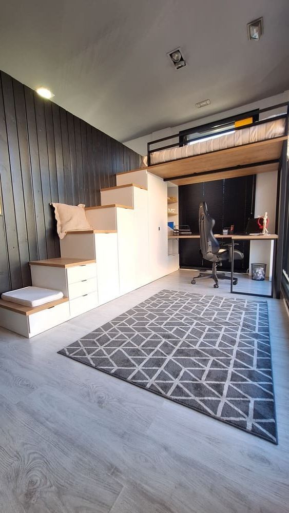 Cama alta con escaleras sobre escritorio, alfombra gris sobre piso de madera clara, habitación moderna y pequeña.