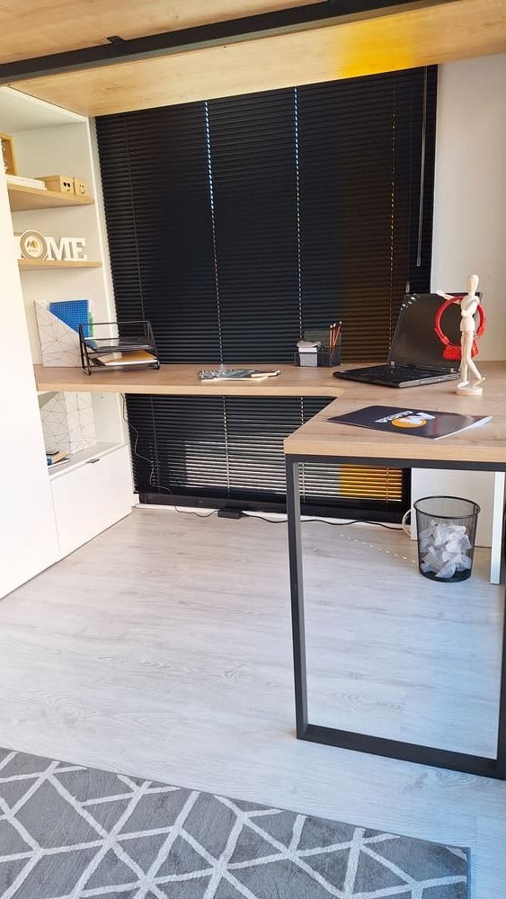 Escritorio con portátil, materiales de arte y persianas negras. Suelo gris en tonos neutros.