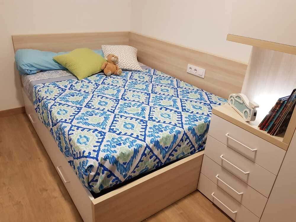 Dormitorio con cama, cajones, almohadas y mesita de noche. Ropa de cama azul y blanca.