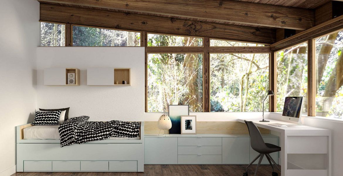 Un dormitorio con una cama, escritorio, silla y muchas ventanas.