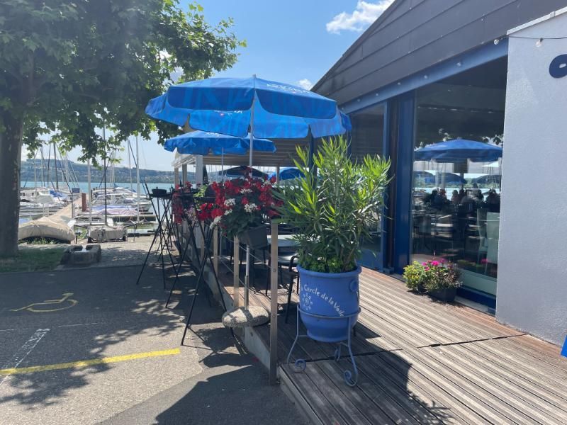 Le restaurant avec des parasols bleus et des plantes en pot devant.