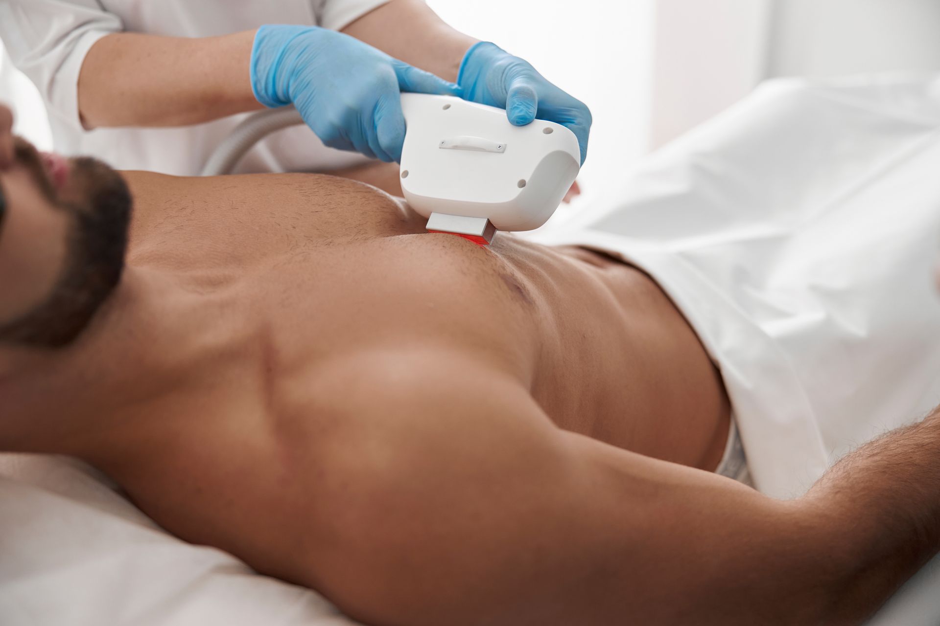 Un clinicien ganté utilise un appareil portatif sur l'abdomen nu d'un patient dans un environnement médical.