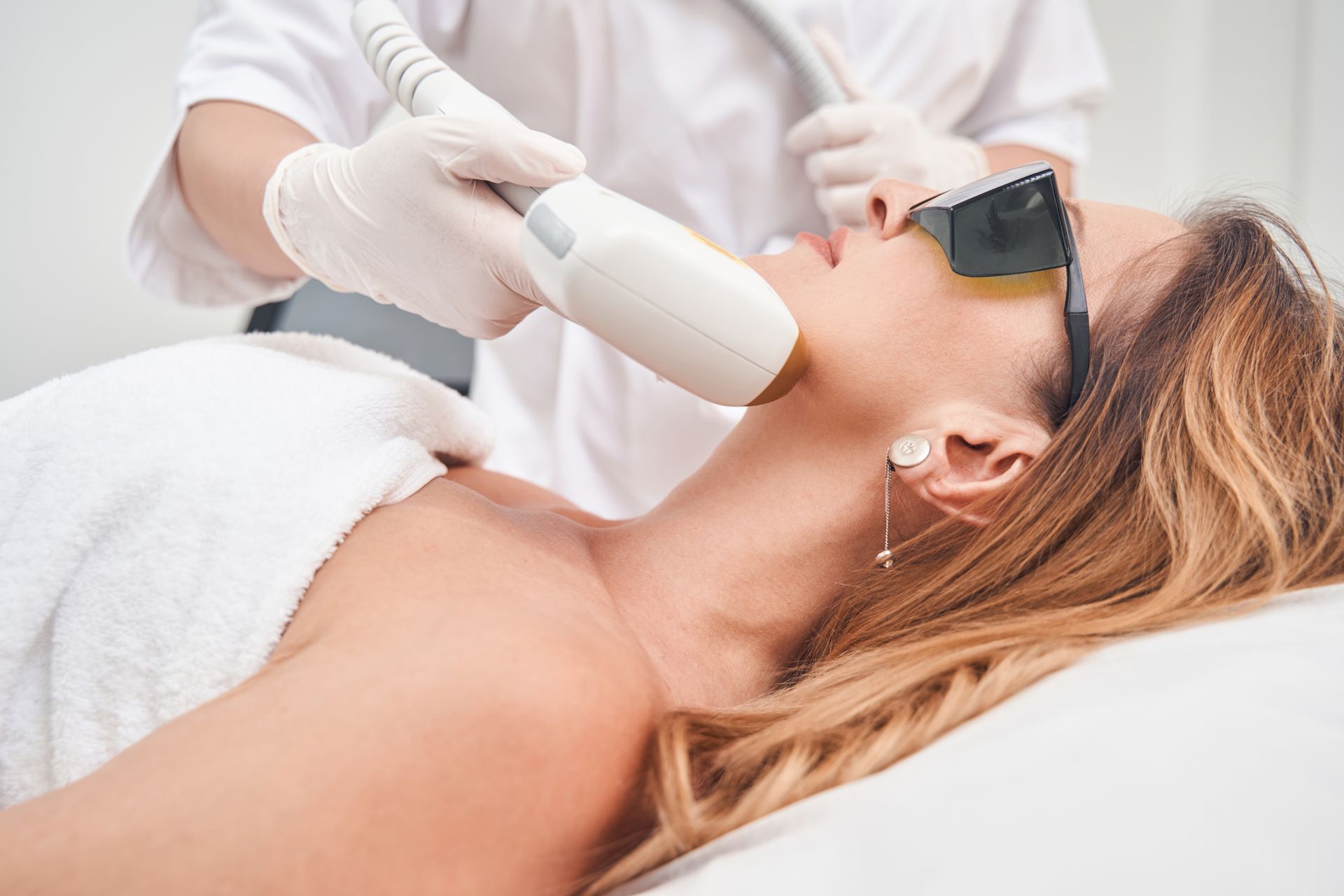 Une femme reçoit un soin du visage tout en portant des lunettes de protection sur un lit.