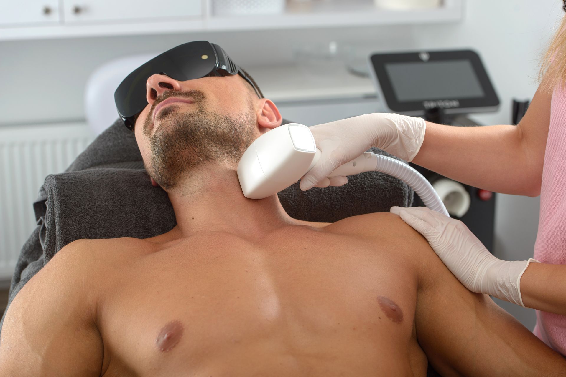 Un homme est allongé sur le dos lors d'une échographie cervicale en clinique, un technicien tenant la sonde.