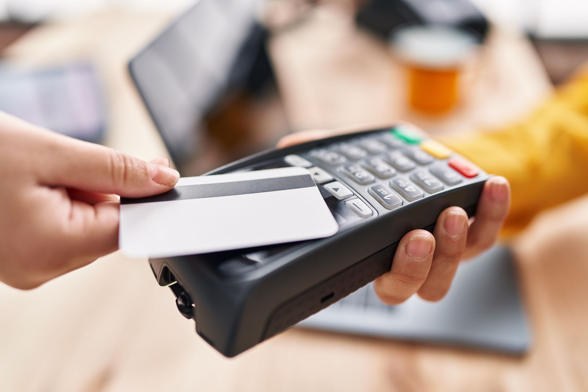 Main tenant une carte de crédit près d'un terminal de paiement avec clavier et écran.