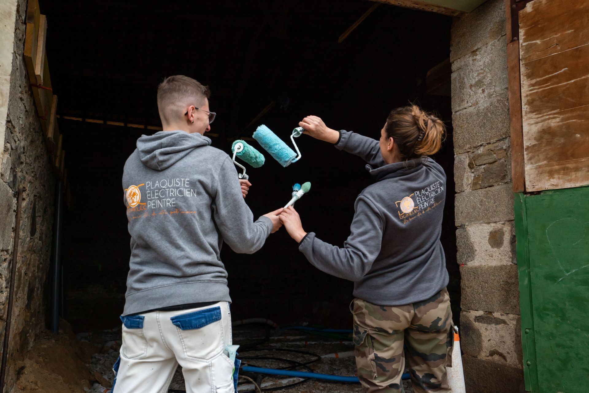 Deux femmes artisans de dos levant leurs pinceaux et rouleaux à peinture
