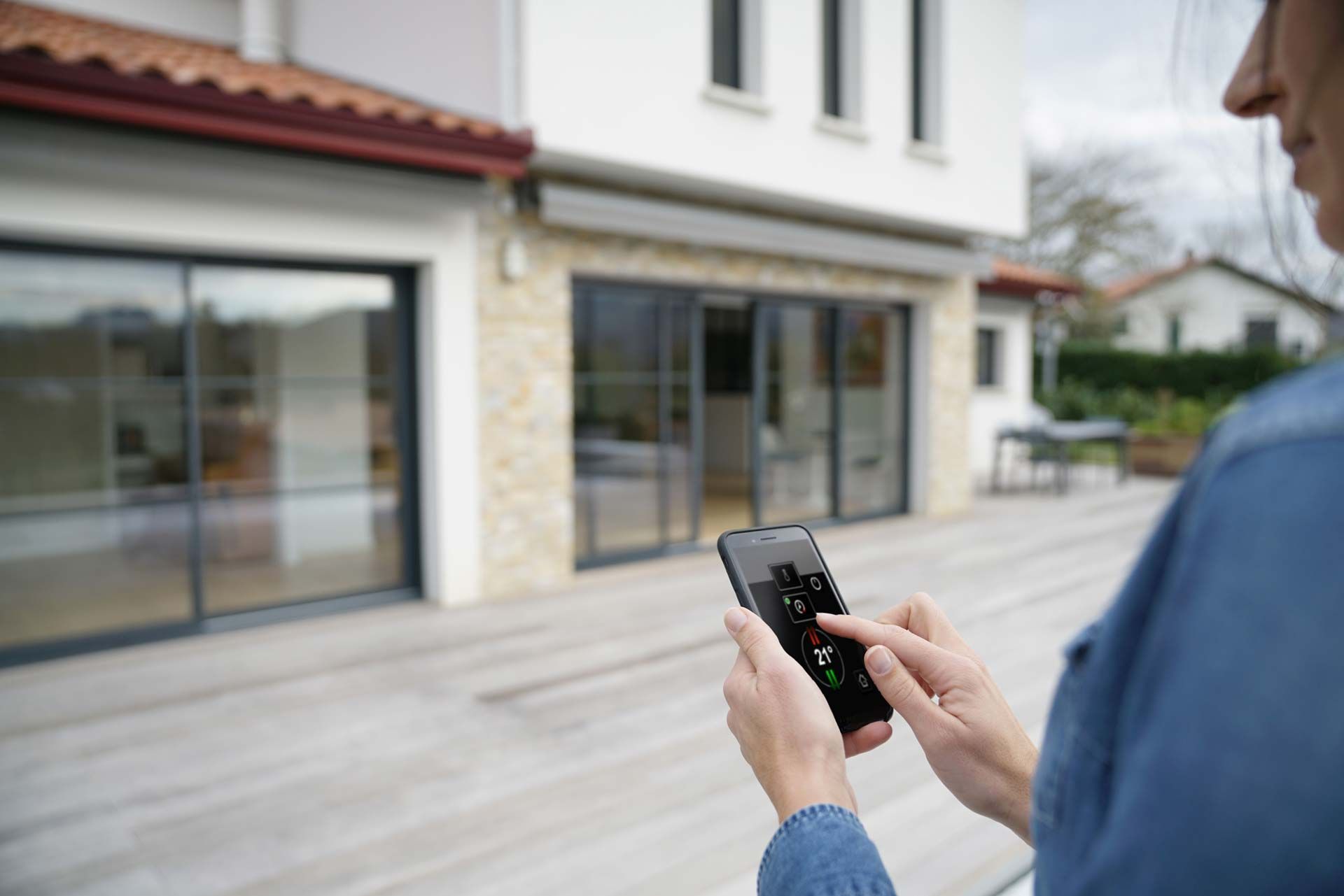 Femme sur sa terrasse utilisant son smartphone pour gérer la fermeture de ses volets roulants