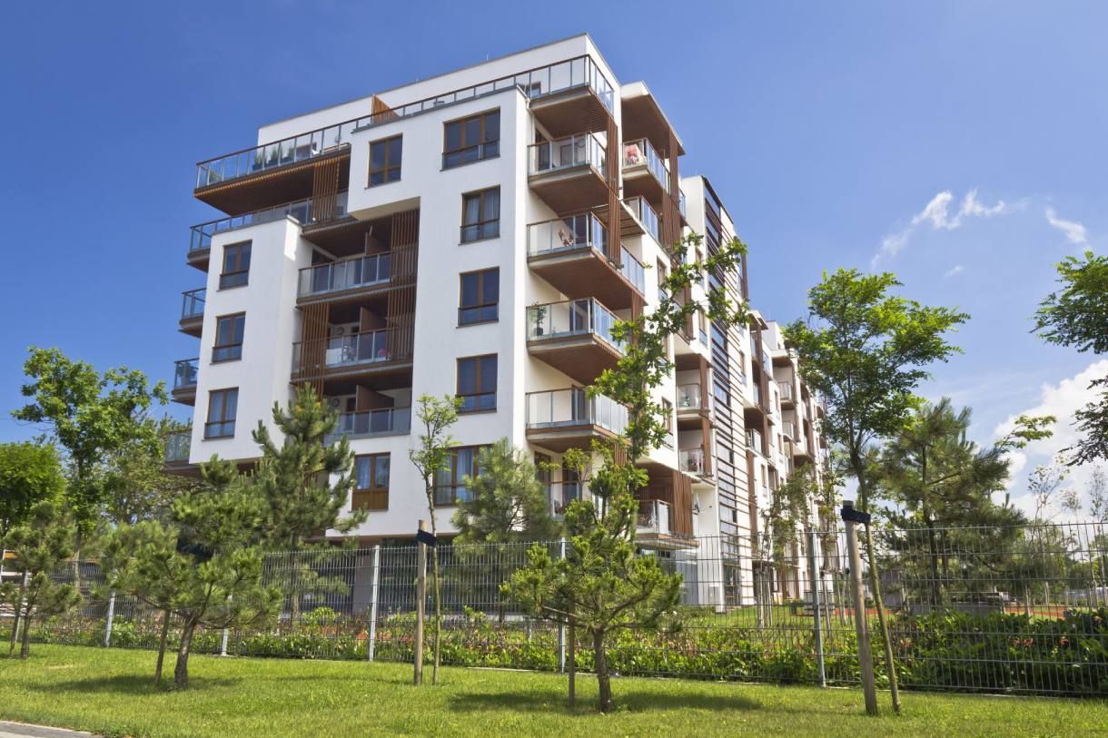 Immeuble d'appartements blanc moderne avec balcons au milieu d'un aménagement paysager verdoyant sous un ciel d'un bleu éclatant