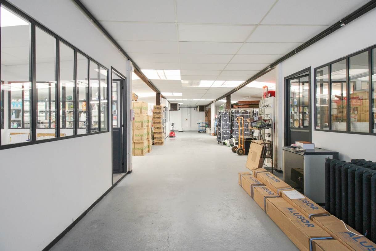 Allée lumineuse d'un entrepôt avec des bureaux vitrés, des étagères et des cartons empilés sous des néons