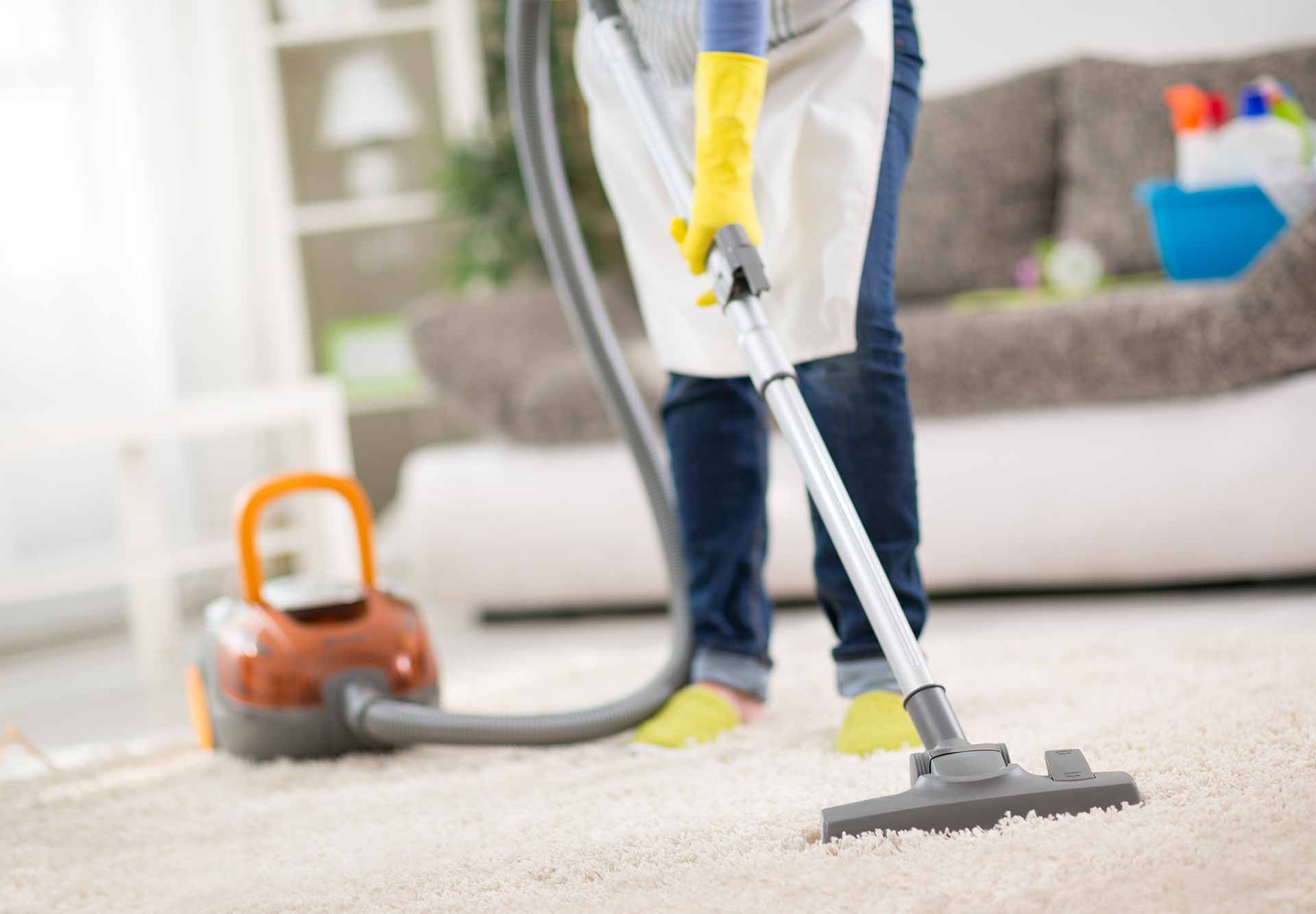 Personne passant l'aspirateur sur un tapis blanc avec un aspirateur traîneau dans un salon lumineux