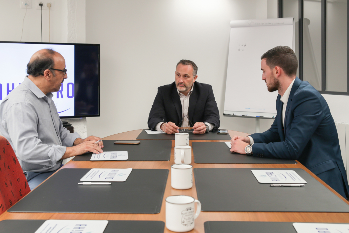 Trois personnes assises autour d'une table dans une salle de conférence pendant une réunion.