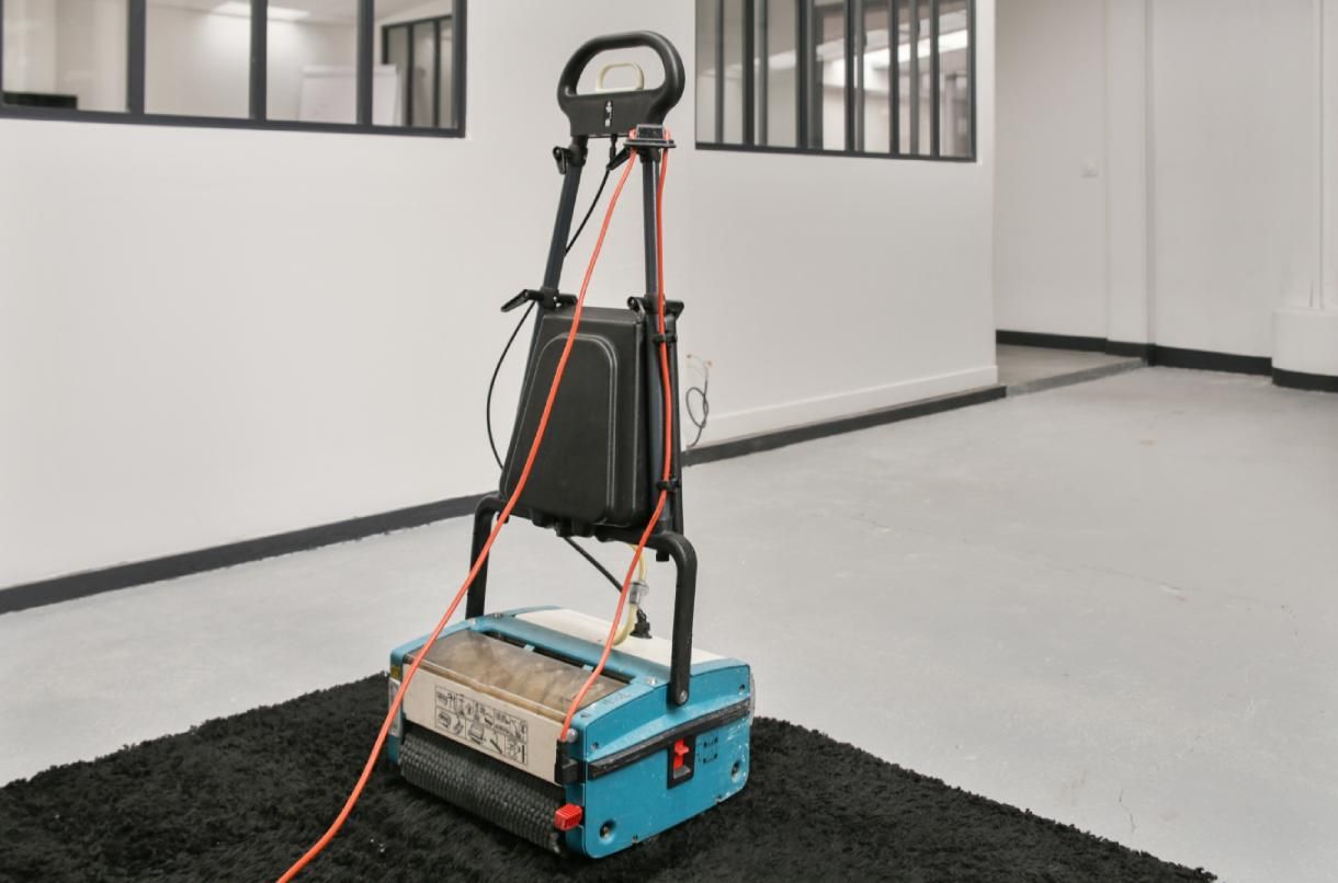 Petit chariot à roulettes avec des câbles orange, dans une pièce intérieure dépouillée, sur un tapis noir.