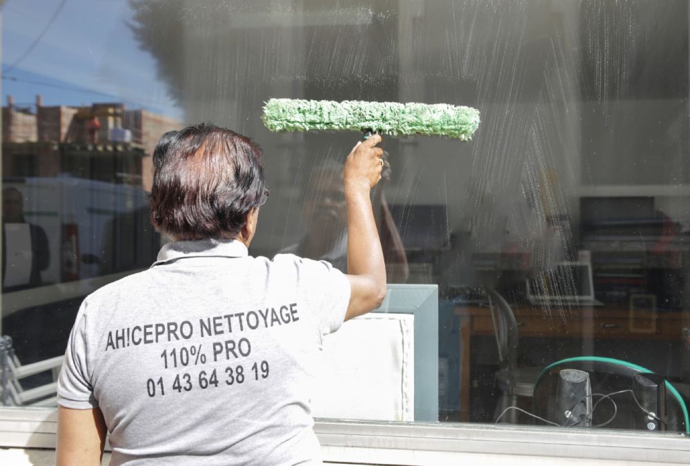 Un laveur de vitres utilise une raclette verte sur la vitrine d'un magasin.