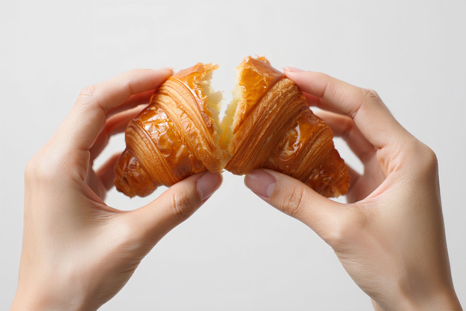 Des mains ouvrent un croissant doré en deux, révélant son intérieur feuilleté.