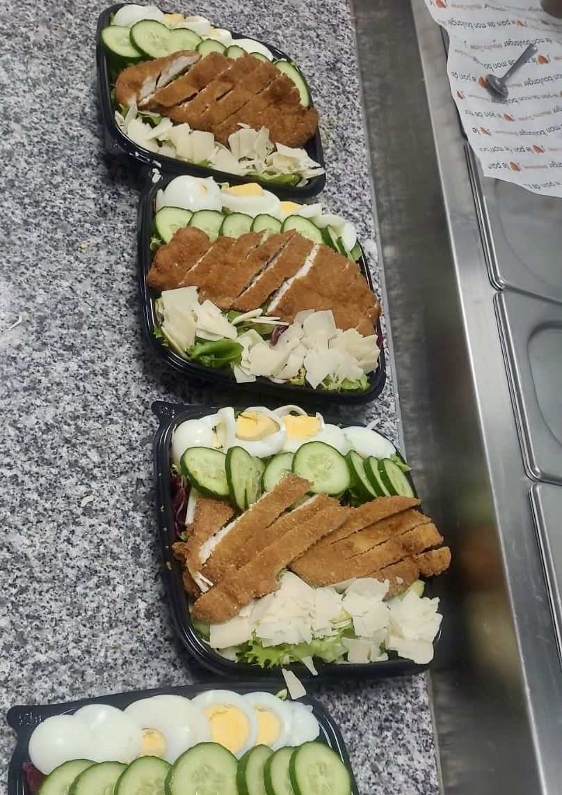 Un chef emballe un sandwich sur une planche en bois, avec de la roquette en arrière-plan.