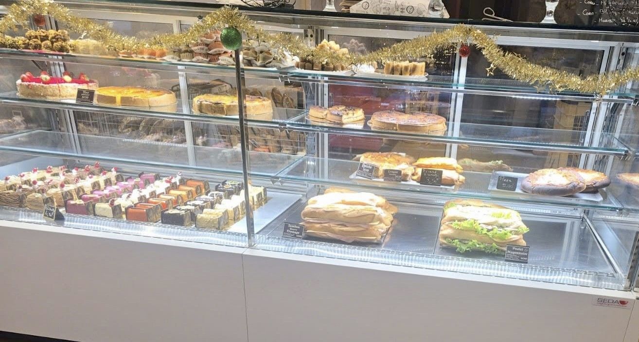 Gâteaux présentés dans une vitrine en verre ; saveurs variées avec garnitures aux fruits et glaçage au chocolat.