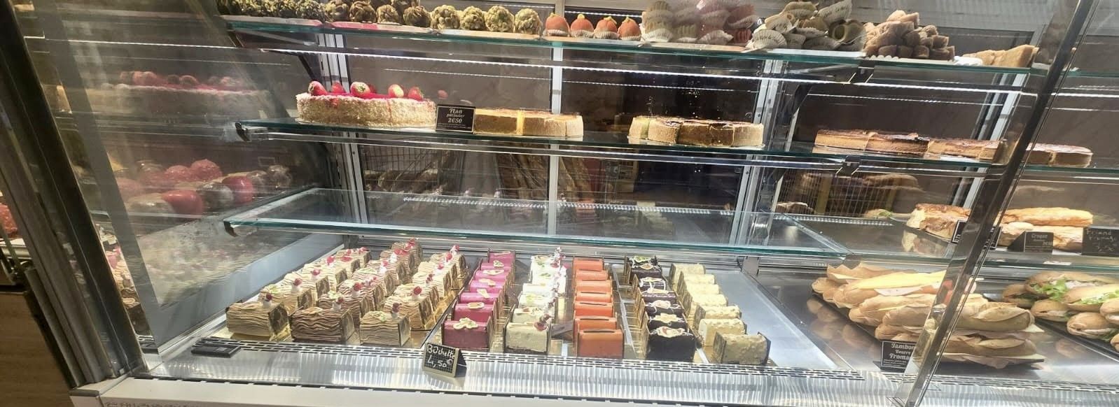 Un assortiment de pâtisseries colorées est présenté dans une vitrine, comprenant des tartes aux fruits et des gâteaux à étages.