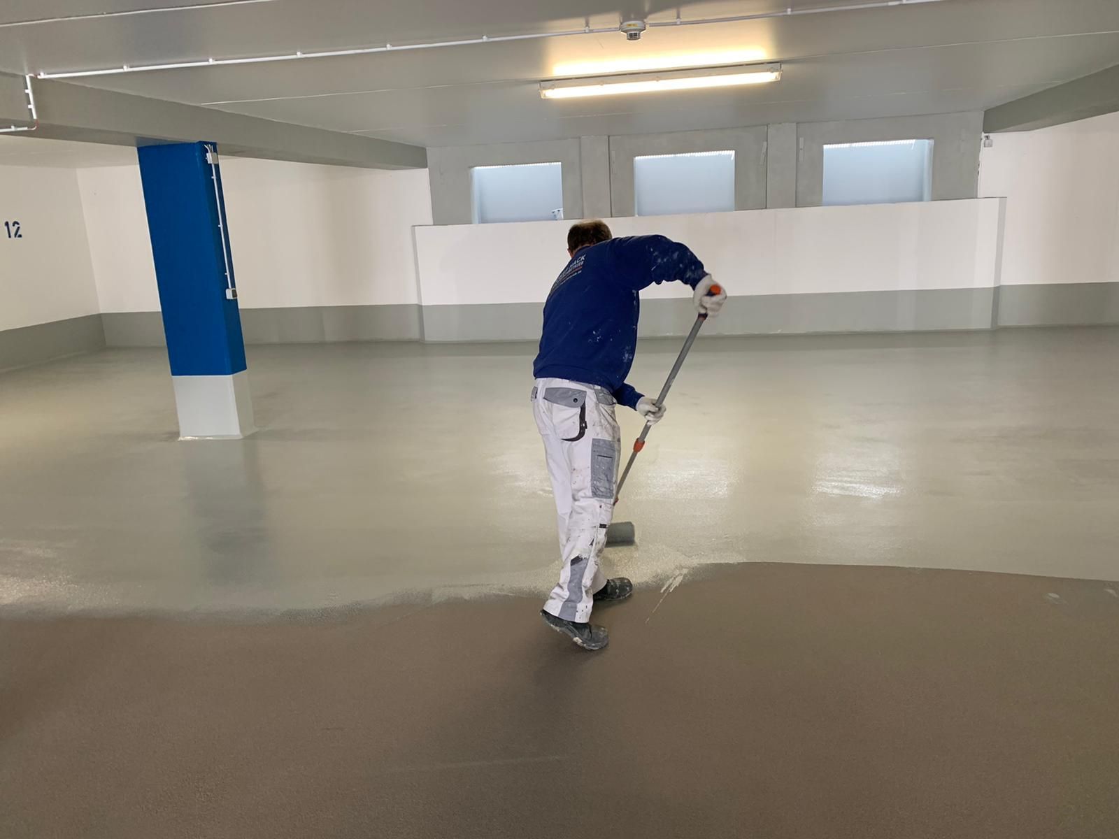 Handwerker bei der Bodenbeschichtung in einer großen Halle.