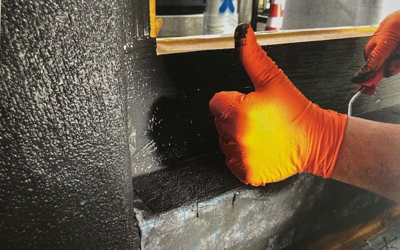 Hand mit Handschuh gibt „Daumen hoch“ vor einer schwarzen Abdichtungsbahn.