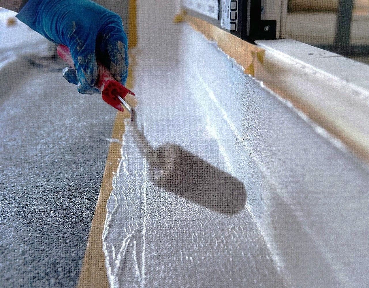 Arbeiter trägt mit einer Kelle Dichtmasse in einer weißen Rinne auf.