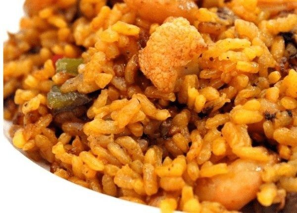 Primer plano de un plato de arroz dorado con camarones y pimientos verdes visibles.