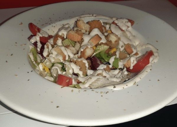 Ensalada en recipiente blanco, cubierta con crutones y aderezo cremoso.