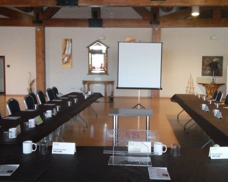 Sala de conferencias con mesas dispuestas para una reunión, pantalla de proyección y obras de arte en las paredes.