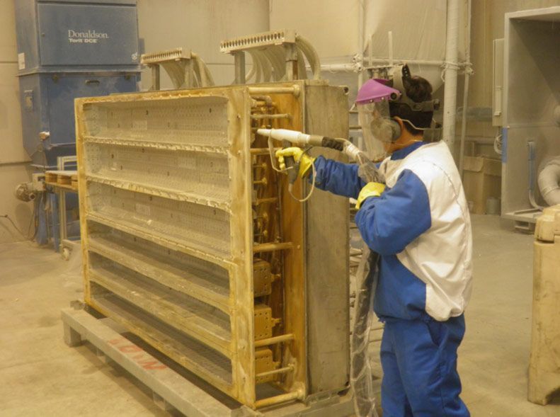 Un hombre que lleva una máscara está pintando un trozo de metal en una fábrica.