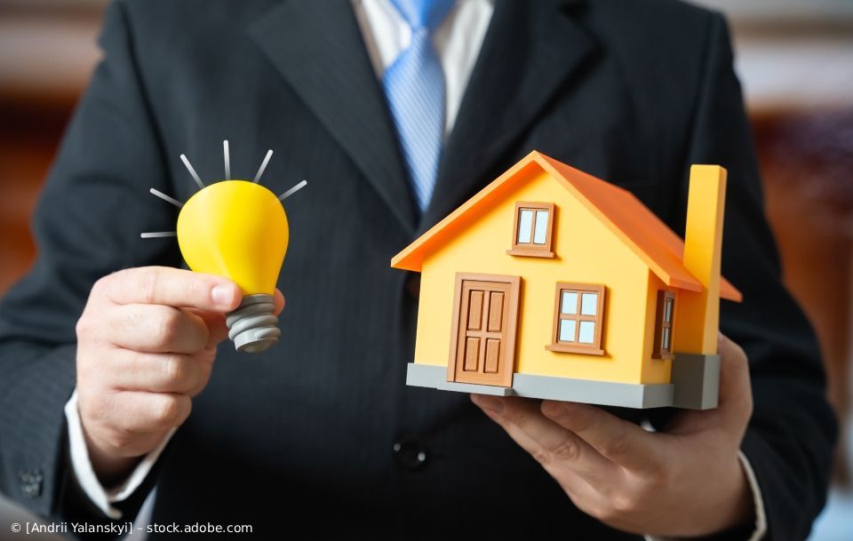 Ein Mann im Anzug hält eine Glühbirne und ein Spielzeughaus in der Hand; 